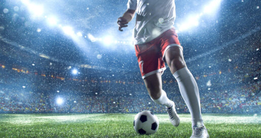 Torso of an athlete kicking a soccer ball in a stadium.