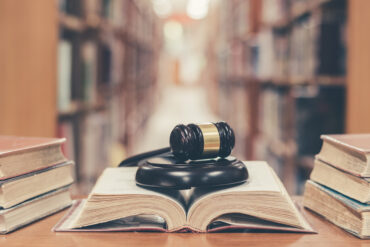 A book sits open on a table in a library with a gavel laying across it.