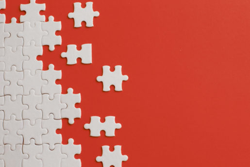 White puzzle pieces are scattered against an orange background with about 90 percent of them fitted together on the left side.