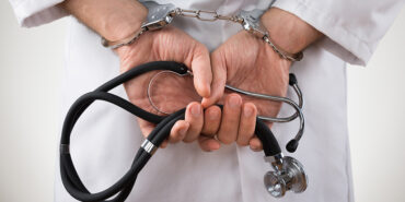 This image shows a set of handcuffed hands holding a stethoscope.