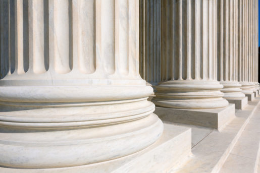 The bottom of the U.S. Supreme Court which showcases classical Corinthian architectural style columns, meaning simple lines around the base (horizontal) and vertical up to the top.
