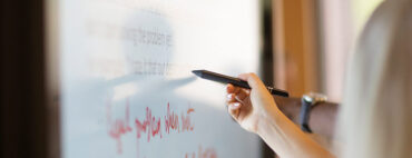 A hand writes on a digital screen in red ink.
