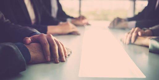 a long shot of looking down a board room table with different hands clasped sitting on the table.