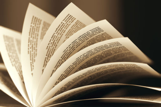 A book is open and the pages are being flipped through while a light shines beneath.