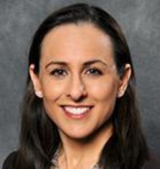 A white woman with brown hair tucked behind her ears smiles widely.