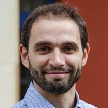 Man in blue shirt with beard smiling.