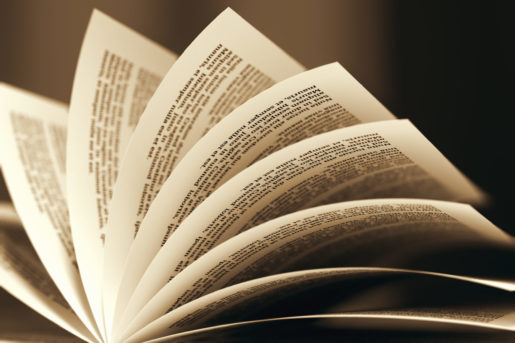 Pages are open and turning in a book with a light shining above.