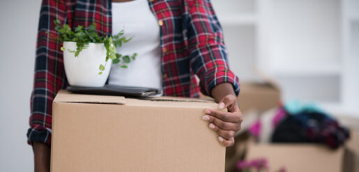 Image of an individual carrying a moving box with a desk plant on top.