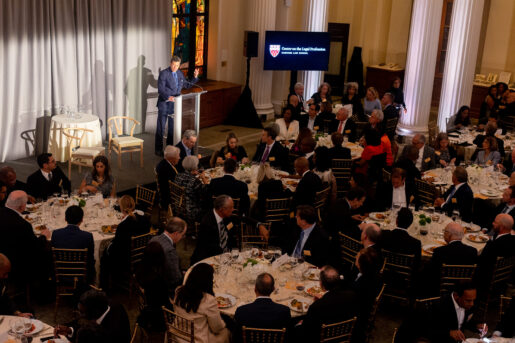 David Wilkins stands on stage in front of a room of individuals eating dinner in formal wear.
