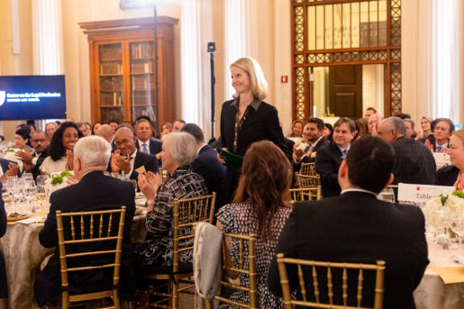 Dana Remus stands as people gaze at her from roundtables.