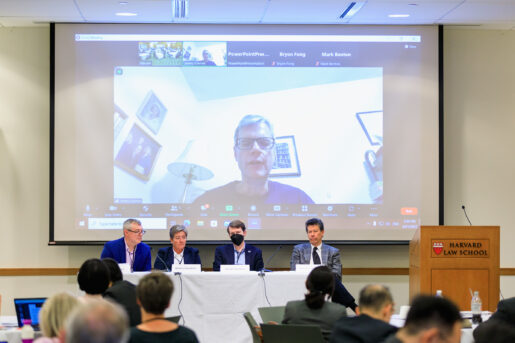 A man speaks via zoom in front of a conference panel.