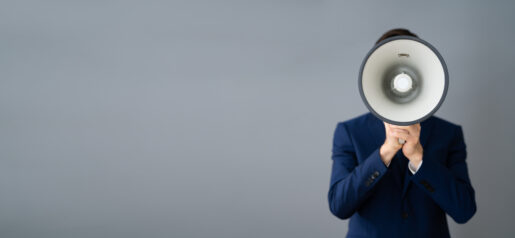 A man in a suit holds a megaphone in front of his face