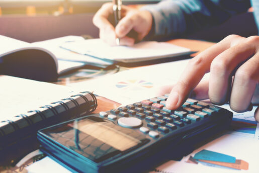 hands of a business person write on paper and punch numbers into a calculator.