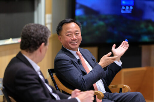 Viet D. Dinh speaks to David Wilkins. Viet smiles and gestures with his hands while the back of David's head is shown.