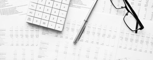 Financial papers, a calculator and a pencil and glasses sit on a desk.
