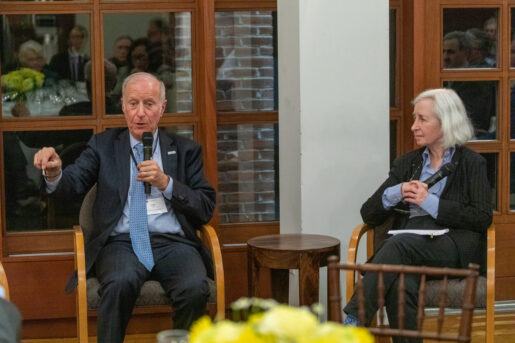 John G. Levi speaks holding a microphone sitting next to Martha Minow.